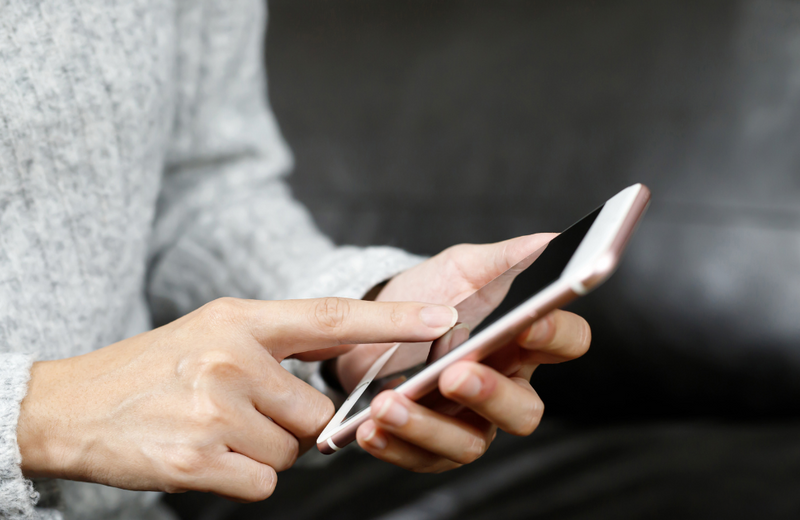 A person in a grey sweater holding a white iPhone 8 in one hand and their finger poised over the screen.