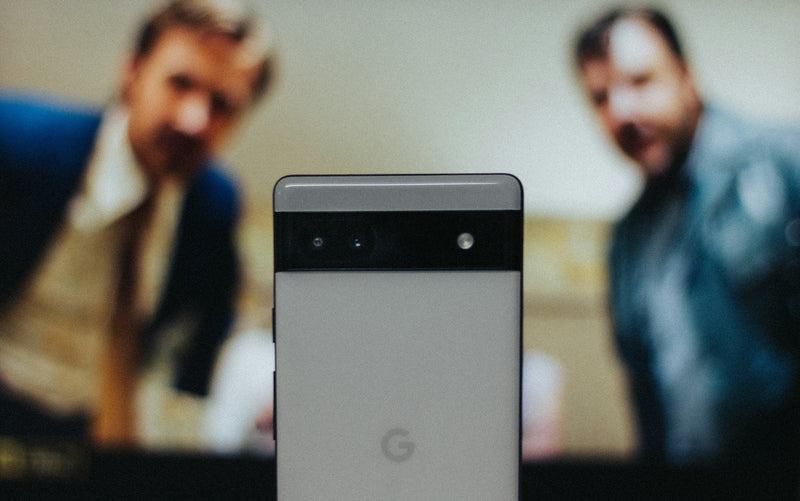 Two men out of focus in the background staring at a Google Pixel phone in the foreground in focus.