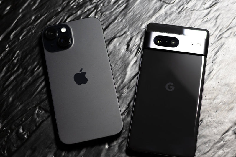 A Google Pixel phone facedown next to an iPhone on a grey slate surface.