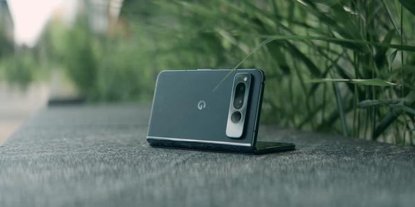 A Google Pixel Fold phone half folded in front of greenery.