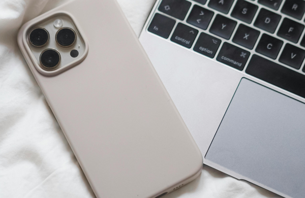 A white iPhone in an ivory case resting facedown on the corner of a MacBook.