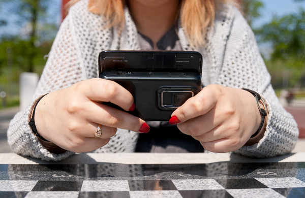 A woman holding an old slide phone from the 90's. Only the back of the phone is visible to the camera. 