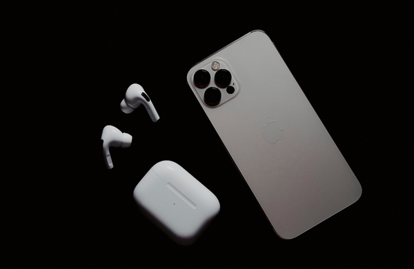 A silver iPhone facedown on a black background next to a pair of Air Pods.